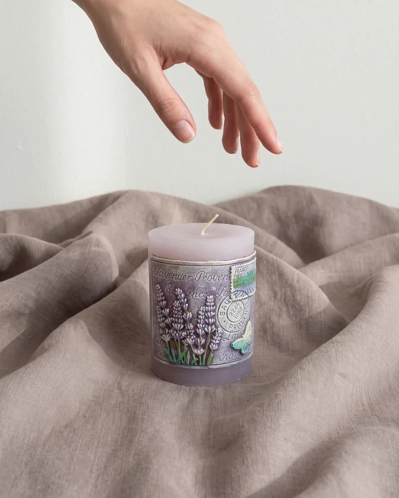 The lilac pillar candle on folds of taupe linen, a hand reaching down towards it, made with Nano Banana 2.